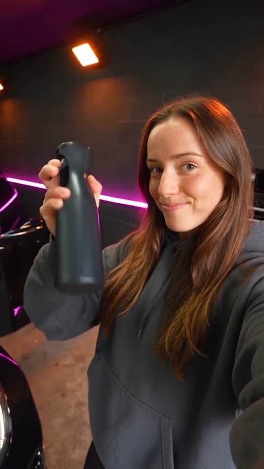 A creator sprays care product onto the hood of a black car and wipes it to a shine.